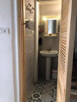 Un baño pequeño con lavamanos pedestal, espejo y baldosas de suelo estampadas.