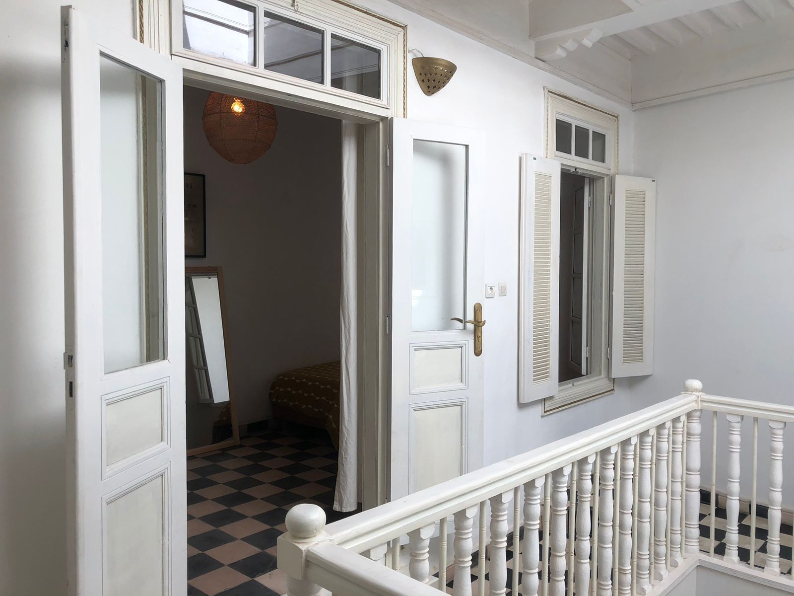 A hallway with a checkered floor, white walls, and a white railing.