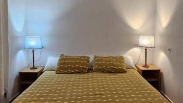 A small, single-bed room with a patterned bedspread, two bedside lamps, and a sloped ceiling.