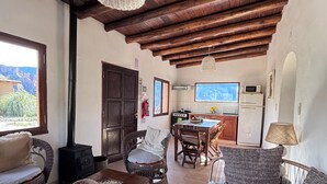 Una sala de estar acogedora con techo de madera, muebles de mimbre y vista a la cocina al fondo.