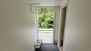 Un couloir avec un tapis à motifs, un banc et une porte donnant sur un espace extérieur doté d’une terrasse en bois.