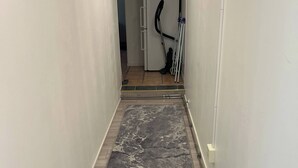 Un couloir étroit, avec un tapis à motifs de marbre gris, un plancher en bois et une porte blanche au fond.