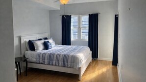 A bedroom with a bed, a nightstand, a ceiling fan, and a window with curtains. - Located in the heart of Ocean City,Downtown this spacious 4-bedroom apartment. (Ocean City)
