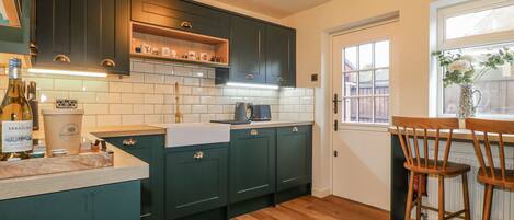 A kitchen with dark green cabinets, a wooden countertop, a sink, and a window with a view.