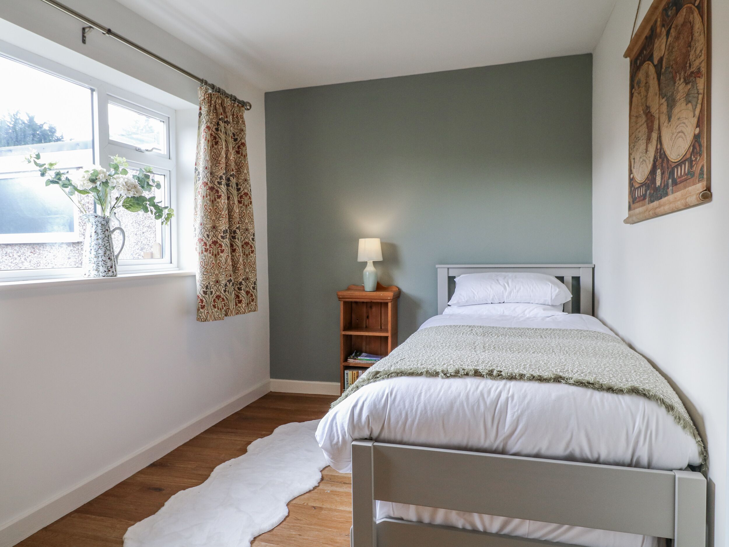 A bedroom with a bed, a window with curtains, a lamp, and a wall-mounted map.