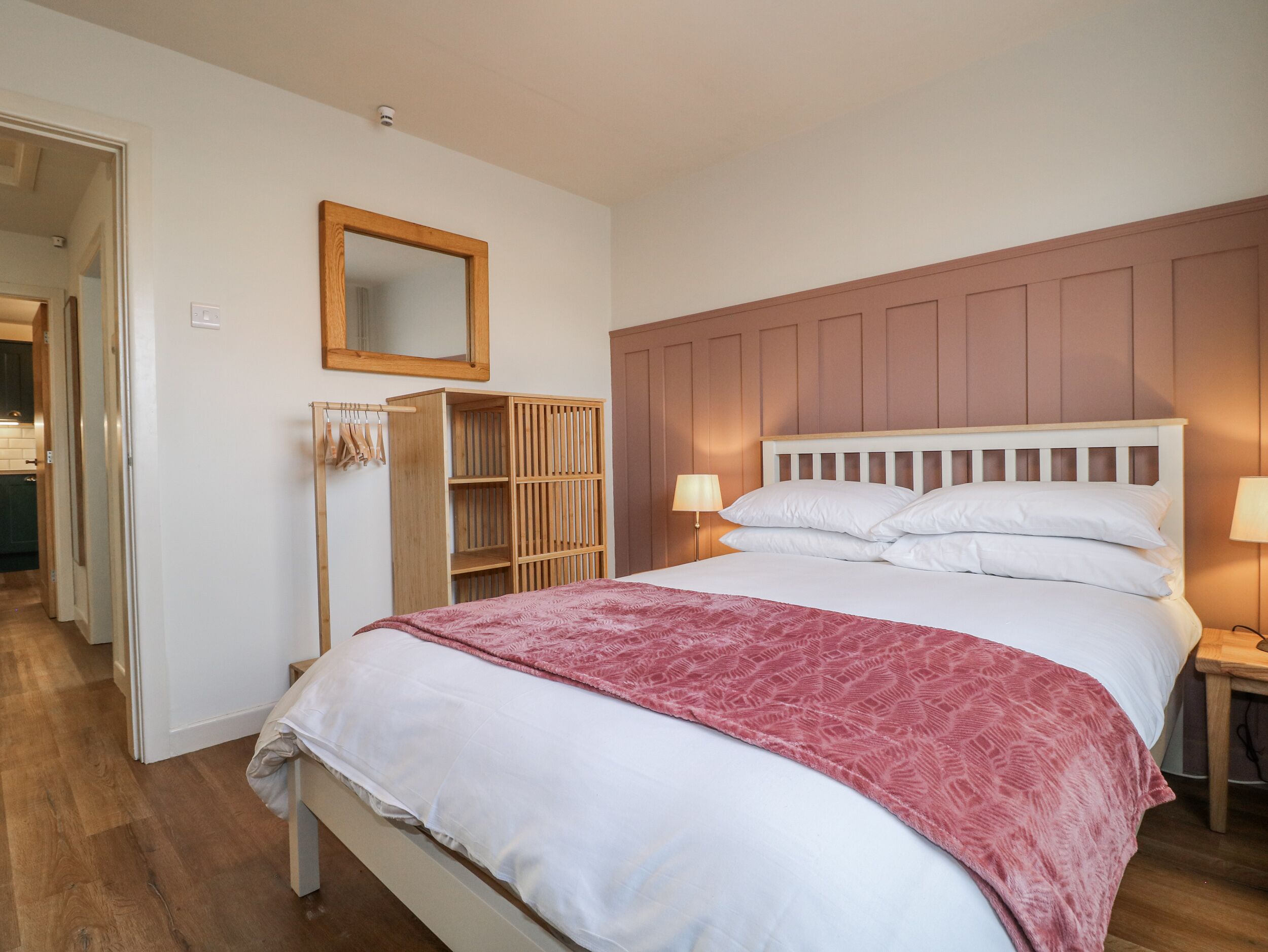 A bedroom with a wooden bed, a bedside table with a lamp, a wardrobe, and a mirror on the wall.