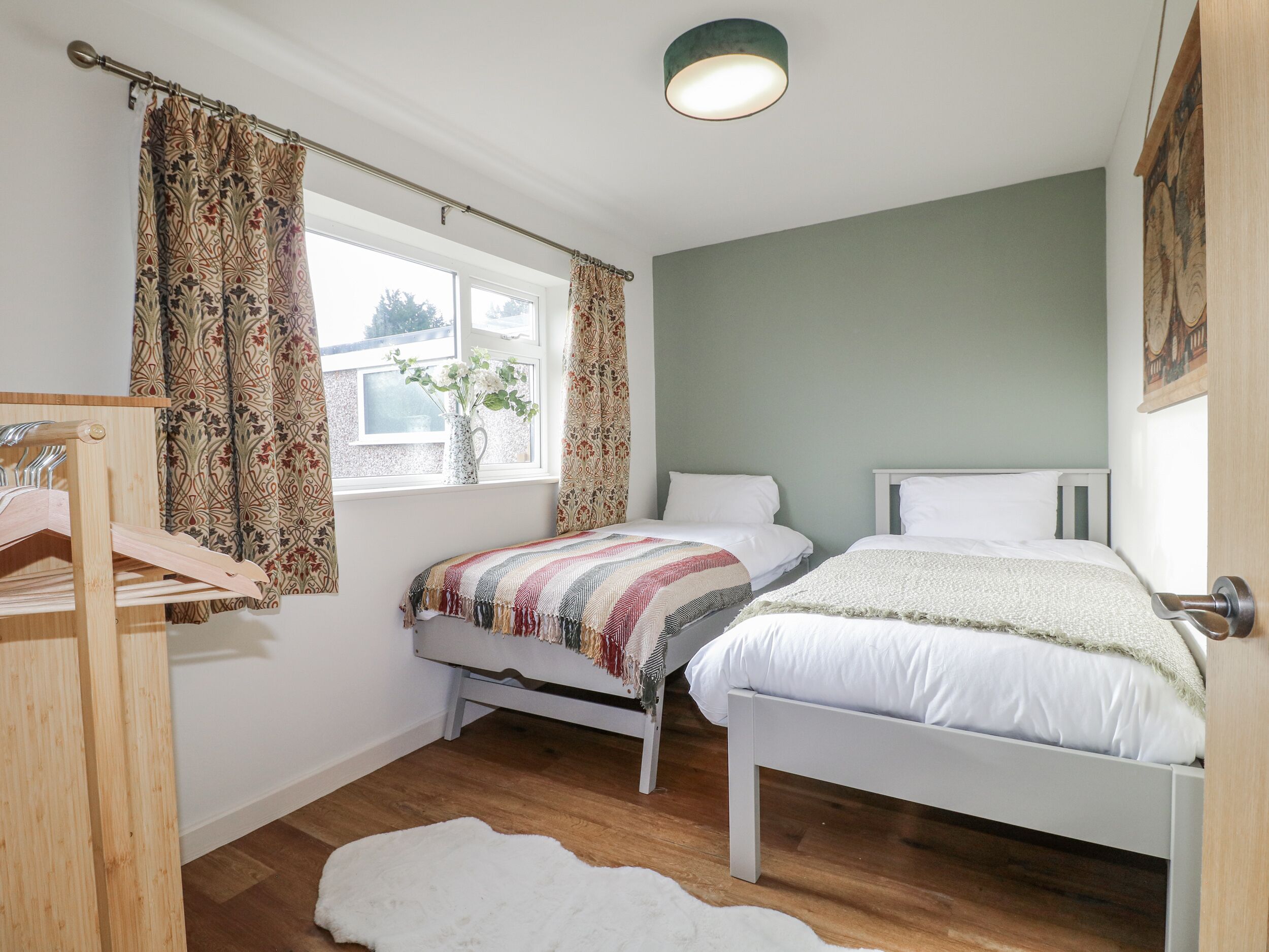 Une chambre avec deux lits, une armoire en bois, une fenêtre avec des rideaux et un luminaire.