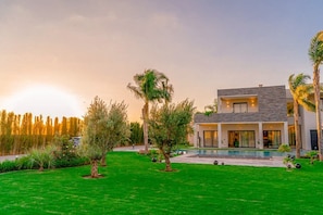 A modern two-story house with a swimming pool, surrounded by a well-maintained lawn and palm trees. - Villa Lumeria (Marrakech)