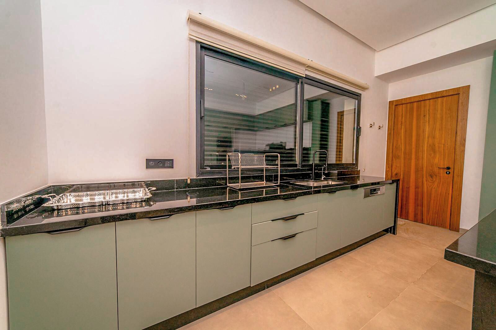 A modern kitchen with a large window, a built-in oven, and a wooden door.