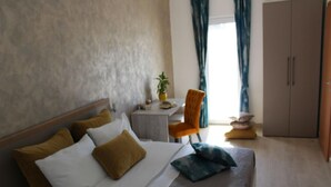 Quarto de hotel com cama, uma pequena mesa, uma cadeira laranja e um guarda-roupa.