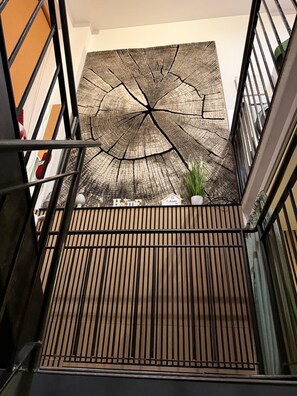 A staircase with a wooden railing and a large, textured wall art piece above. - Andreas Apartments (Berlin)