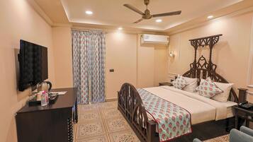 A hotel room with a bed, a desk with a television, a ceiling fan, an air conditioning unit, and a patterned floor.