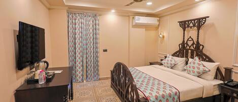 A hotel room with a bed, a desk with a television, a ceiling fan, an air conditioning unit, and a patterned floor.