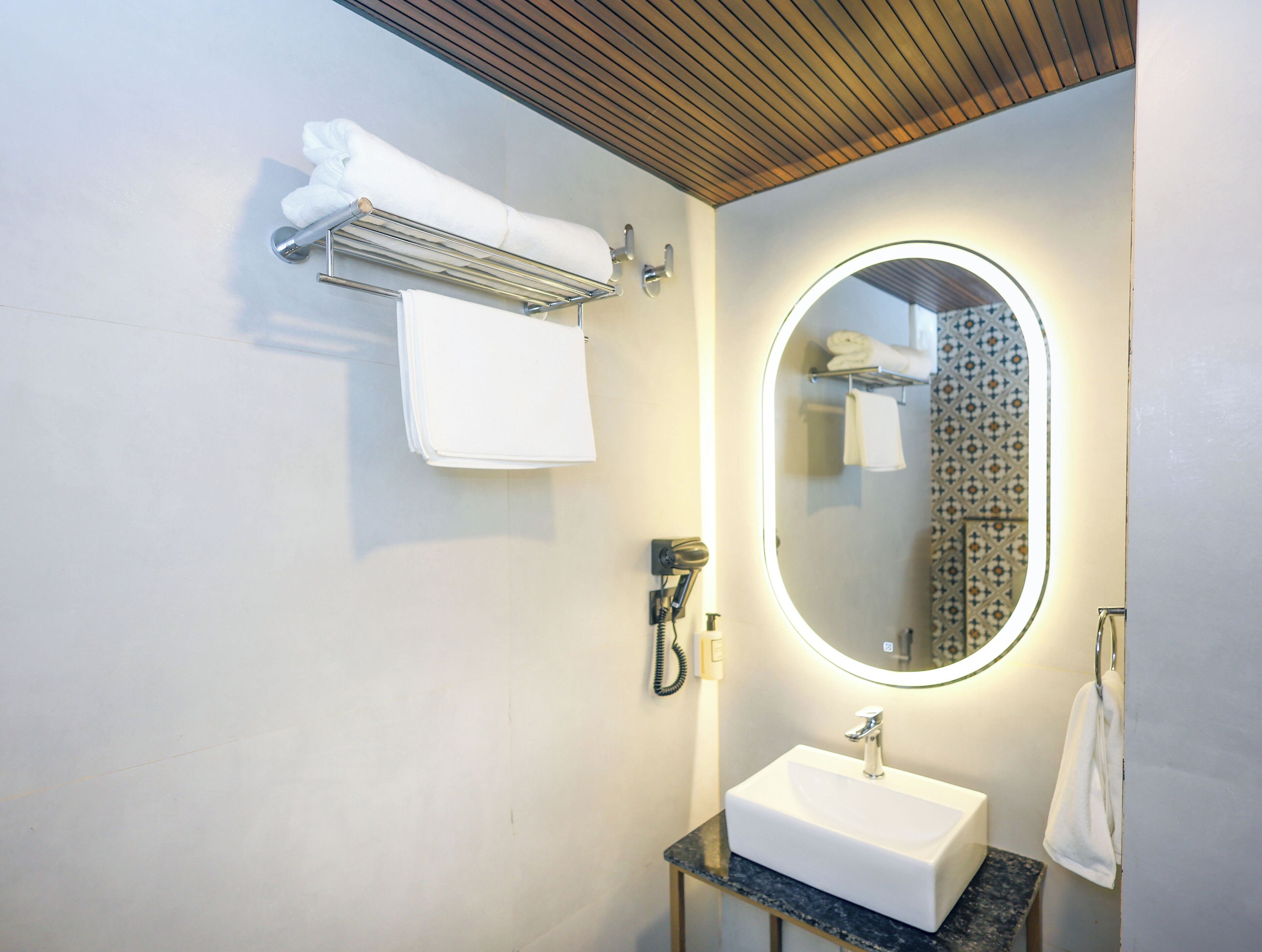 A modern bathroom with a white sink, a mirror with a light, and a towel rack.