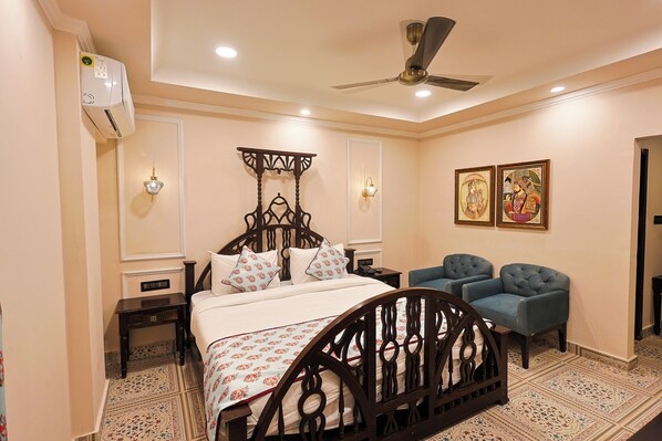 A bedroom with a bed, two chairs, a ceiling fan, and wall-mounted lights. - Ved Mahal (Jaipur)