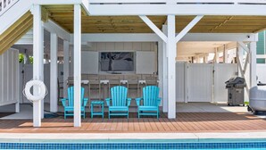 A covered outdoor area with a pool, wooden deck, and two blue Adirondack chairs. - Ultimate Luxury 7-bedroom, 7+bathroom w/private pool &elevator, steps from the beach (Holden Beach)