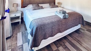 Quarto com teto de madeira, uma cama com peseira, duas mesas de cabeceira e uma mesinha de apoio.