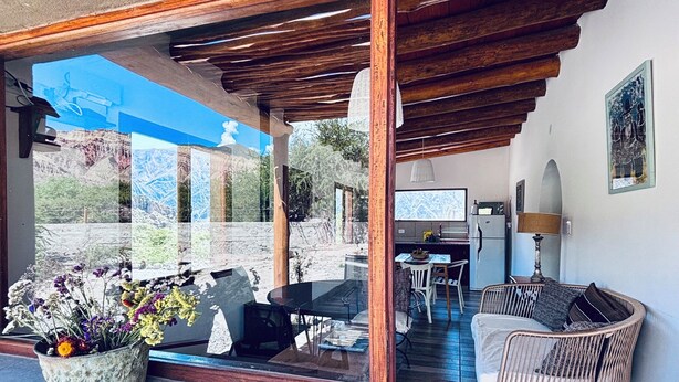 Uma área de estar coberta ao ar livre, com pérgola de madeira, mesa de jantar e sofá de vime.