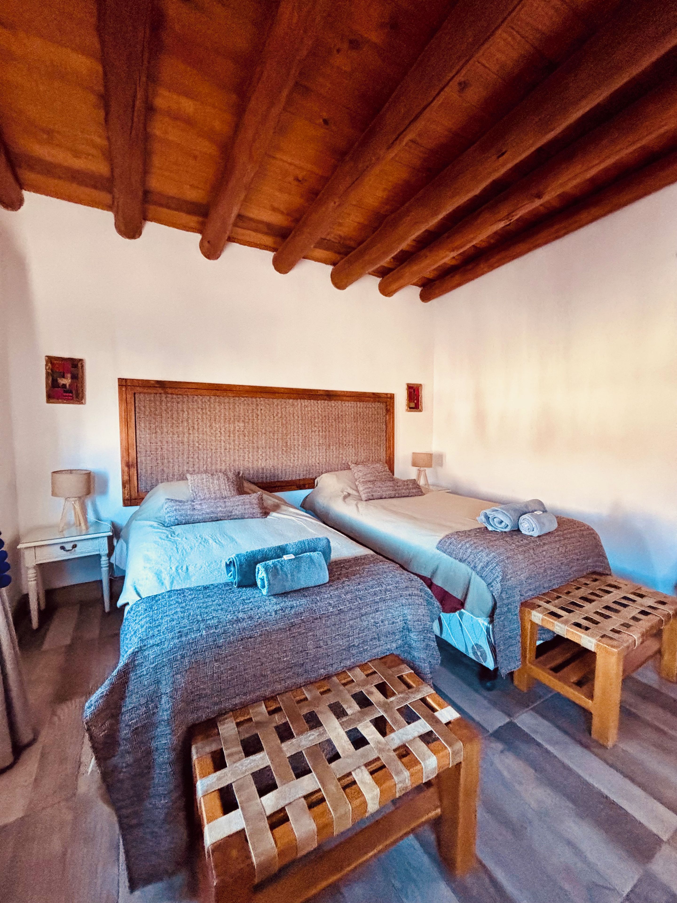 Un dormitorio con dos camas, un banco de madera y una mesita de noche con lámpara.