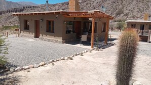 Um edifício rústico com alpendre coberto, base de pedra e um cacto em primeiro plano.