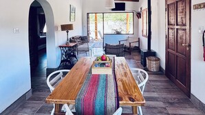 Uma área de jantar rústica com uma mesa de madeira e cadeiras brancas, um cesto de palha e um tapete colorido.