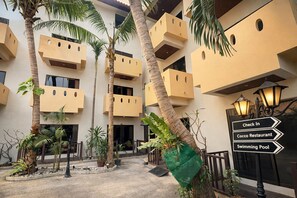 A hotel courtyard with palm trees, a swimming pool, and a sign for the Coco Restaurant. - Akira Resort (Pattaya)