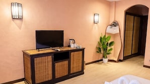 A hotel room with a bed, a television on a wooden cabinet, a potted plant, and a mirror. - Akira Resort (Pattaya)