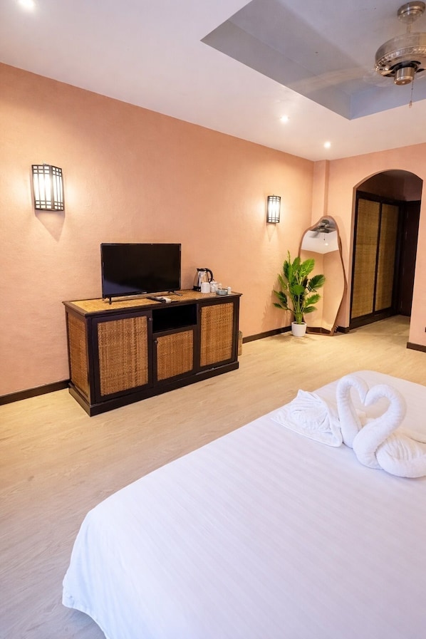 Ein Hotelzimmer mit Bett, Fernseher auf einem Holzschrank, einer Zimmerpflanze und einem Spiegel.
