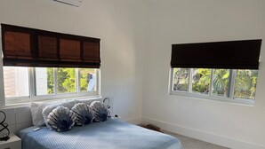 Ein Schlafzimmer mit einem Bett, zwei Fenstern mit Jalousien, einem Nachttisch und einer Heizung.