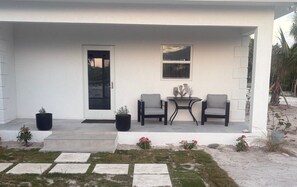 A modern house with a covered porch, two grey chairs, a small table, and potted plants.