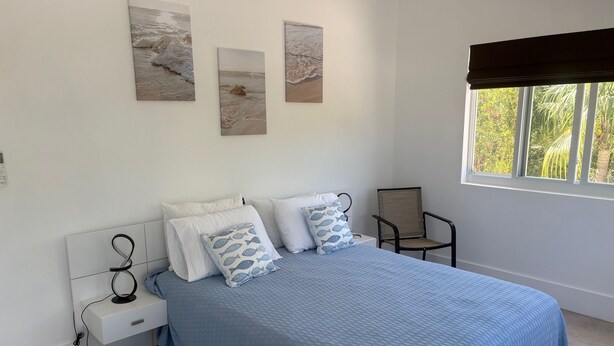 A bedroom with a bed, pillows, a chair, a window, and artwork on the wall.