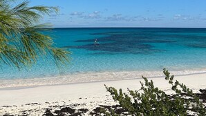 Ein Strand mit klarem türkisblauem Wasser, weißem Sand und einer Person, die auf einem Paddleboard steht.