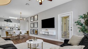 Ein modernes Wohnzimmer mit einer schwarzen Couch, einem weißen Couchtisch und einem Essbereich mit einer weißen Küche im Hintergrund.
