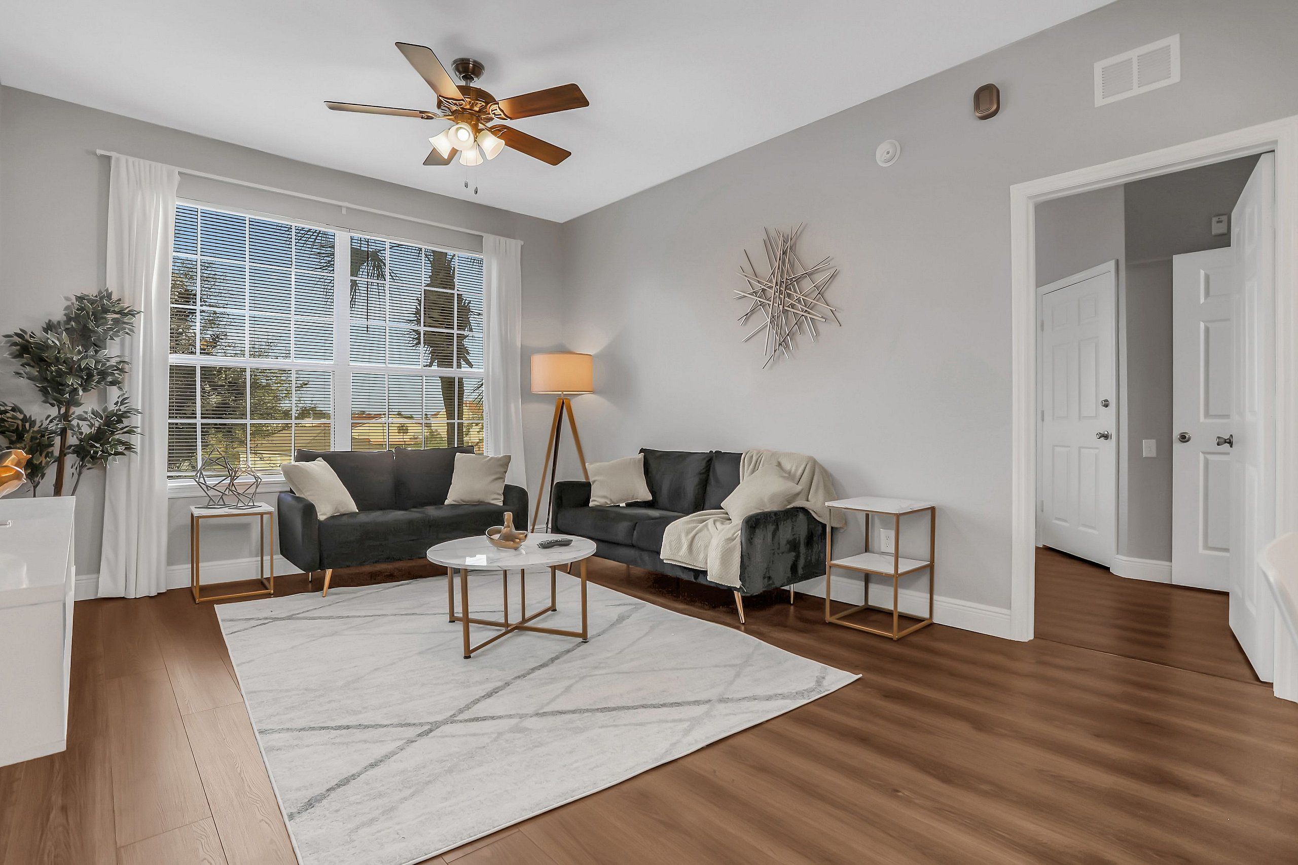A modern living room with a ceiling fan, two sofas, a coffee table, and a large window with blinds.
