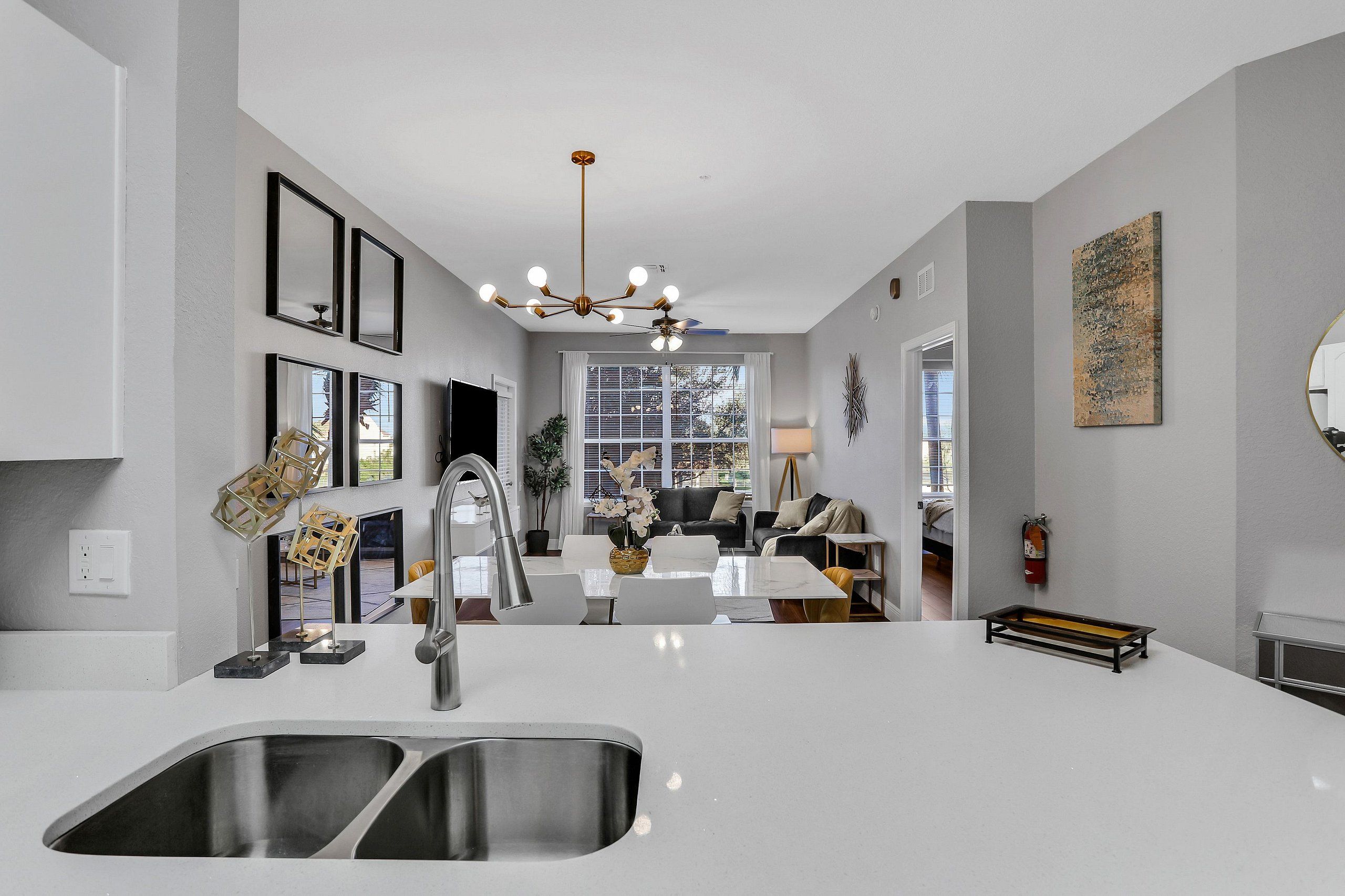 A modern kitchen with a double sink, a chandelier, and a dining area with a white table and chairs.