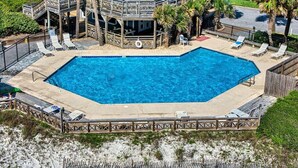 Una piscina rectangular amb una terrassa de fusta i seients de relaxació, envoltada per una zona de platja sorrenca.