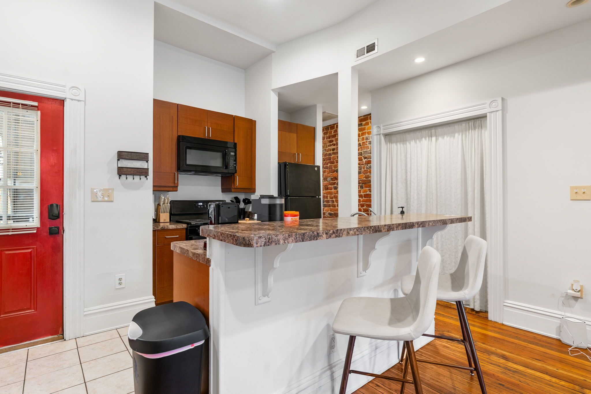 A compact kitchen with a central island, wooden cabinets, and a red door.