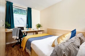 Un dormitorio con cama, escritorio, silla y ventana con cortinas.