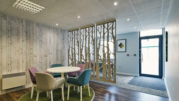 A conference room with a round table, colorful chairs, a wooden partition with tree designs, and a door leading outside. - Ty Willis House (Bangor)