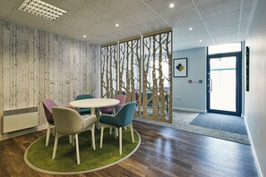 Une salle de conférence dotée d’une table ronde, de chaises colorées, d’une cloison en bois ornée de motifs d’arbres et d’une porte donnant sur l’extérieur.