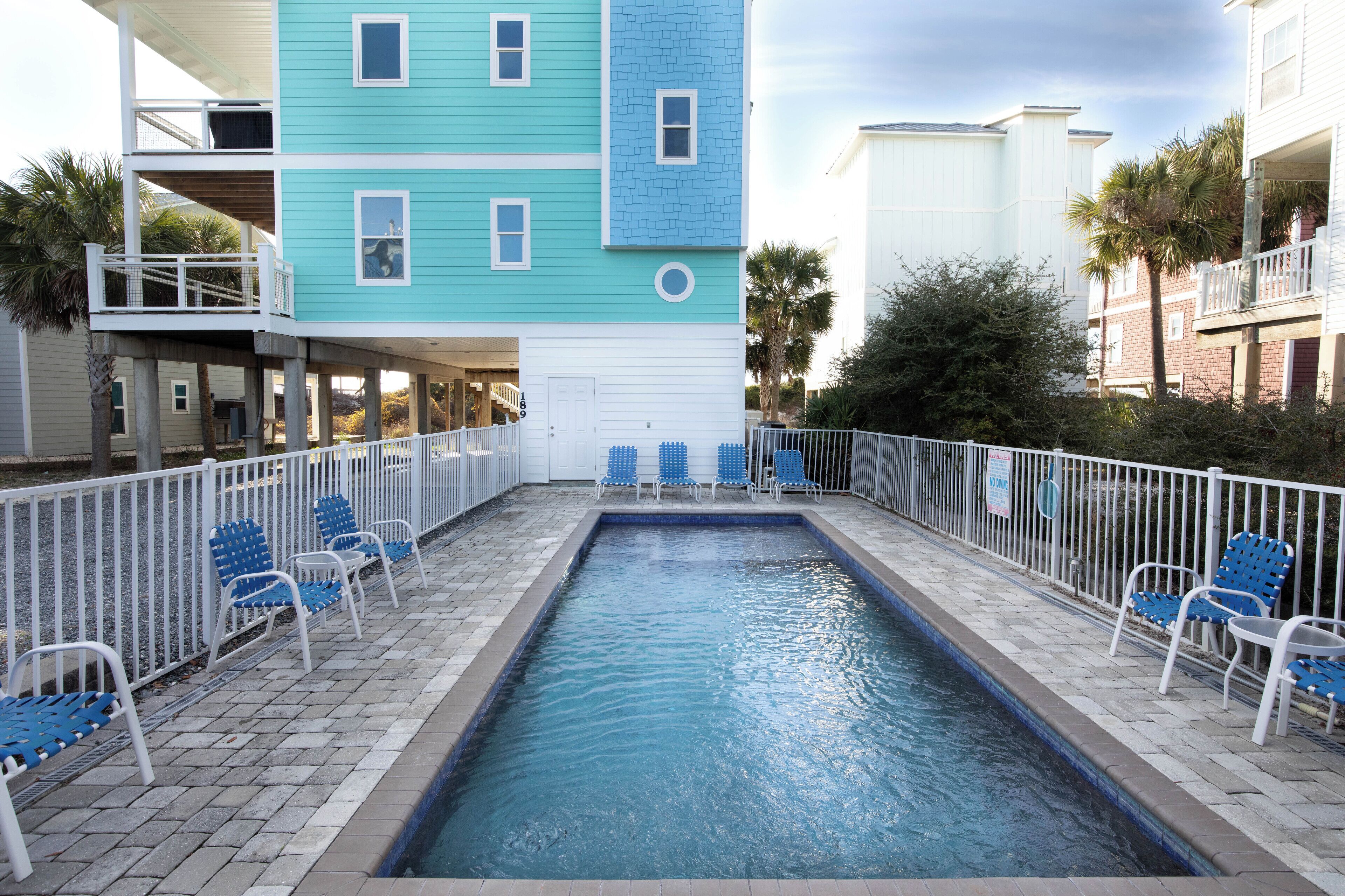A pool area with blue chairs and a small pool, surrounded by a white fence.