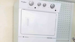 Valkoinen Whirlpool-merkkinen pesukone ja -kuivausrumpu on sijoitettu päällekkäin pyykinhuoneeseen.
