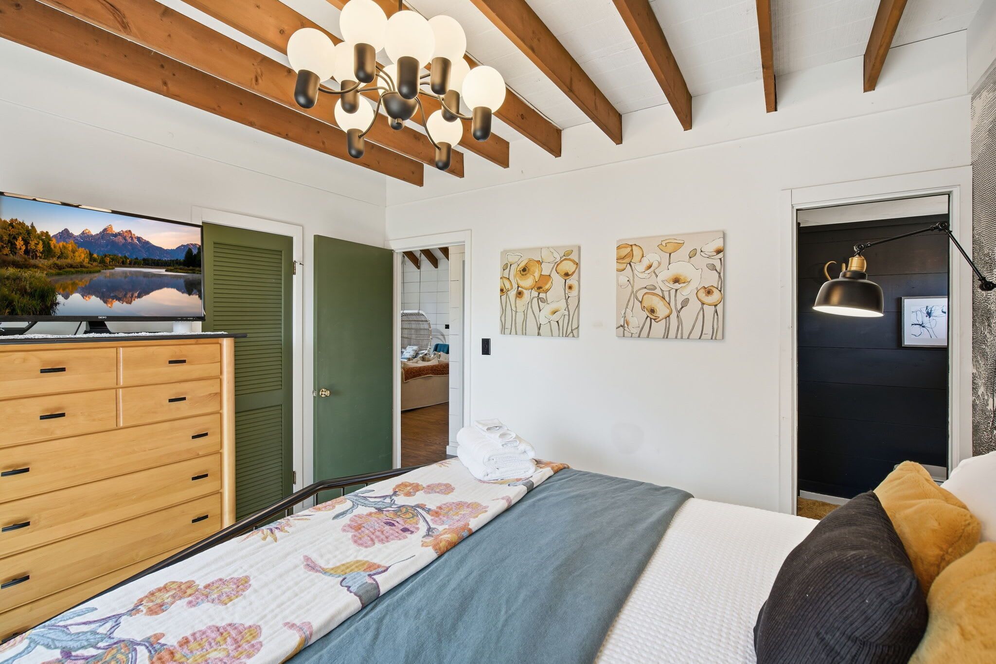 A bedroom with a bed, a wooden dresser, a television, and artwork on the wall.
