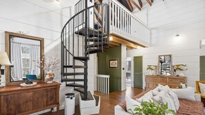 A spacious living room with a wooden floor, a white sofa, a wooden cabinet, and a black spiral staircase leading to an upper level. - Heavenly Mountain Escape in Big Canoe! Golf & Lake (Jasper)