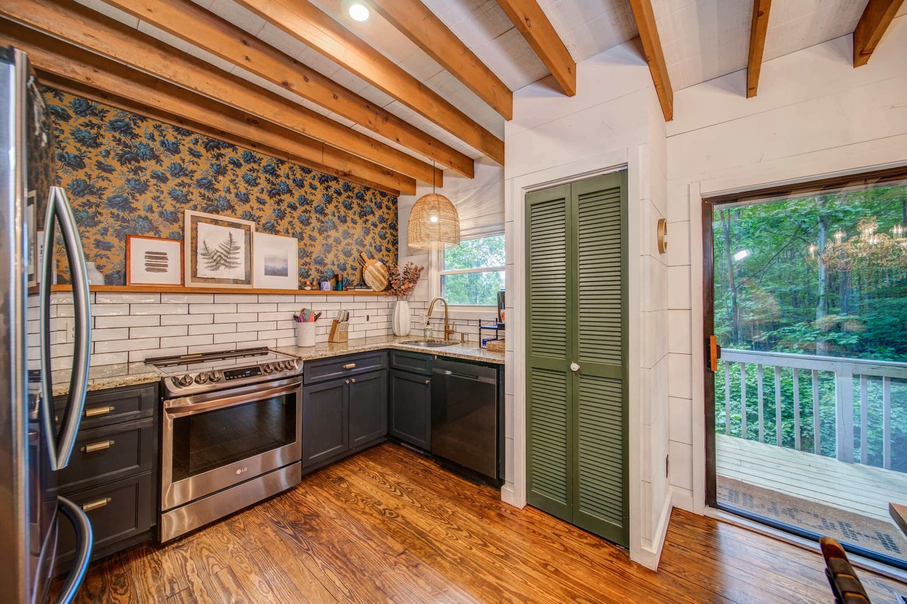 A kitchen with wooden beams, a tiled backsplash, and a view of the forest through a sliding door.