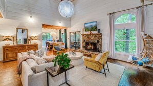 A spacious living room with a fireplace, wooden beams, a dining area, and large windows. - Heavenly Mountain Escape in Big Canoe! Golf & Lake (Jasper)