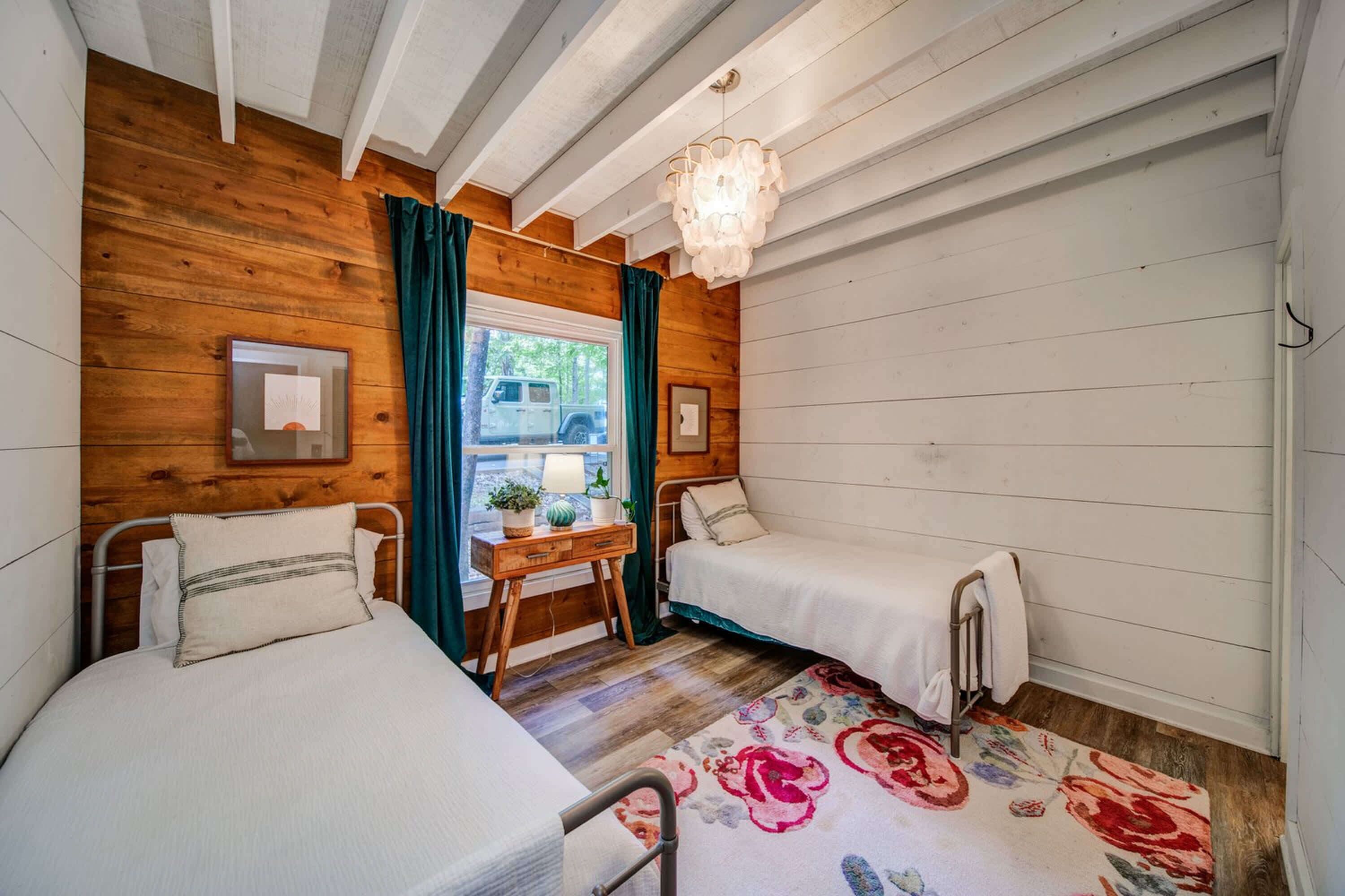 A cozy room with two single beds, a wooden ceiling, a small table with a lamp, and a view of the outdoors.