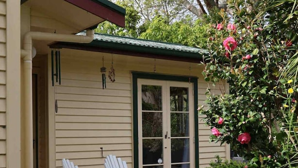 Ein Haus mit einer Veranda, zwei weißen Stühlen und einem kleinen Tisch.