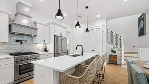 A modern kitchen with white cabinetry, a central island with bar stools, stainless steel appliances, and pendant lighting. - Modern Pet-Friendly Retreat for Families w/2 Bunk Rooms | Brand New Pool! (Seagrove Beach)