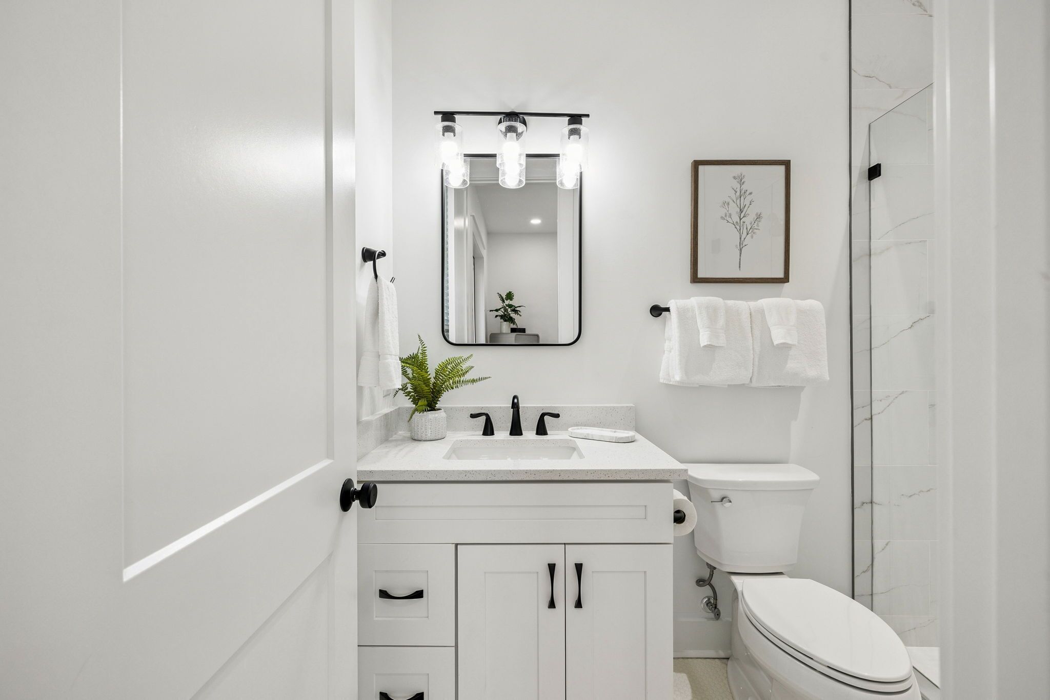 Une salle de bain moderne avec un lavabo blanc, un robinet noir et un miroir avec éclairage intégré. On peut voir les toilettes et l’espace de la douche.